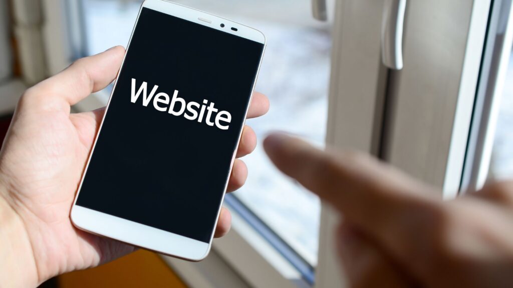 A person holds a smartphone displaying the word "Website" on the screen, while another hand points at the phone near a window, suggesting ideas for animation for website design.