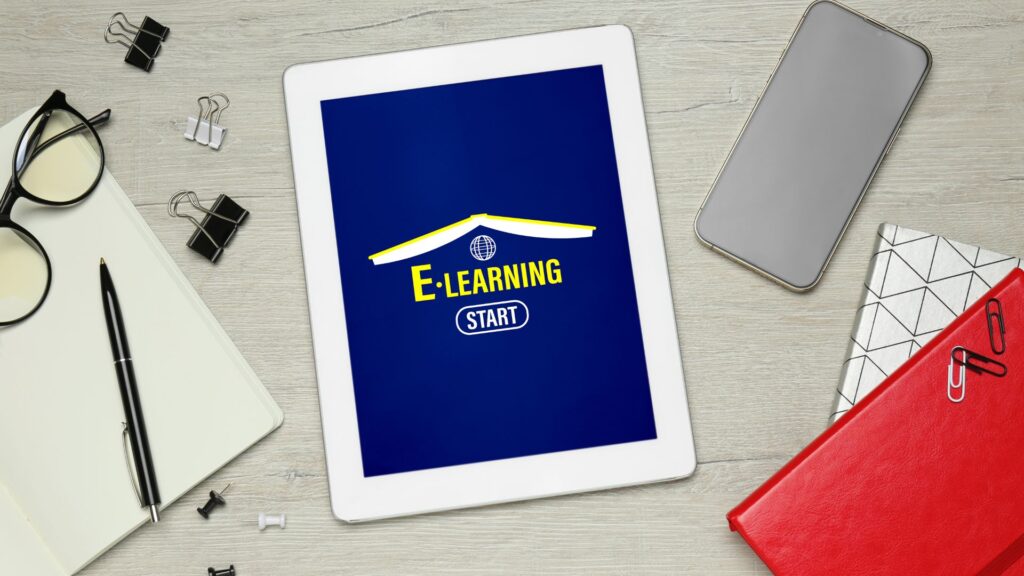 A tablet on a desk displays an E-learning start screen with Online Course Animation. Surrounding items include a smartphone, eyeglasses, pen, paper clips, and notebooks.