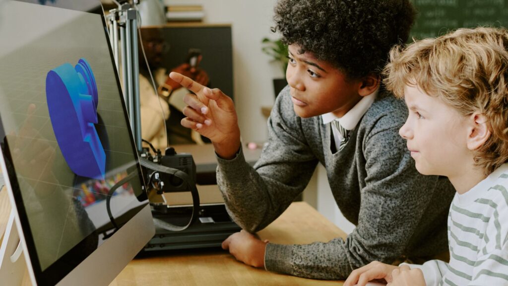 Two children look at a computer screen displaying an educational animation of a 3D model while working together at a desk. One child is pointing at the screen, exploring interactive learning in an engaging environment.