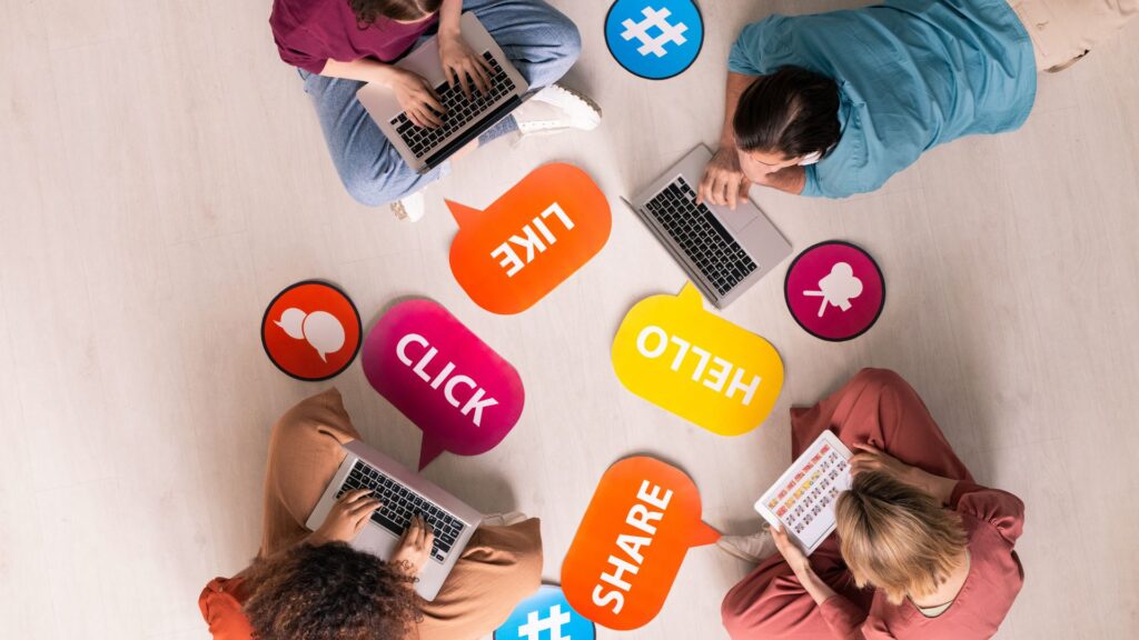 Four people sit in a circle using laptops, surrounded by colorful speech bubbles with words like "LIKE," "CLICK," "SHARE," and "#", creating the perfect scene for an engaging animation for social media.