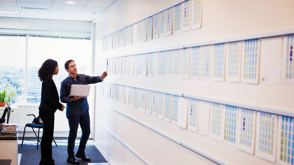 Two people stand in a UK office, reviewing charts on the wall—one holds a laptop and points at the 2025 cost breakdown for explainer video price.