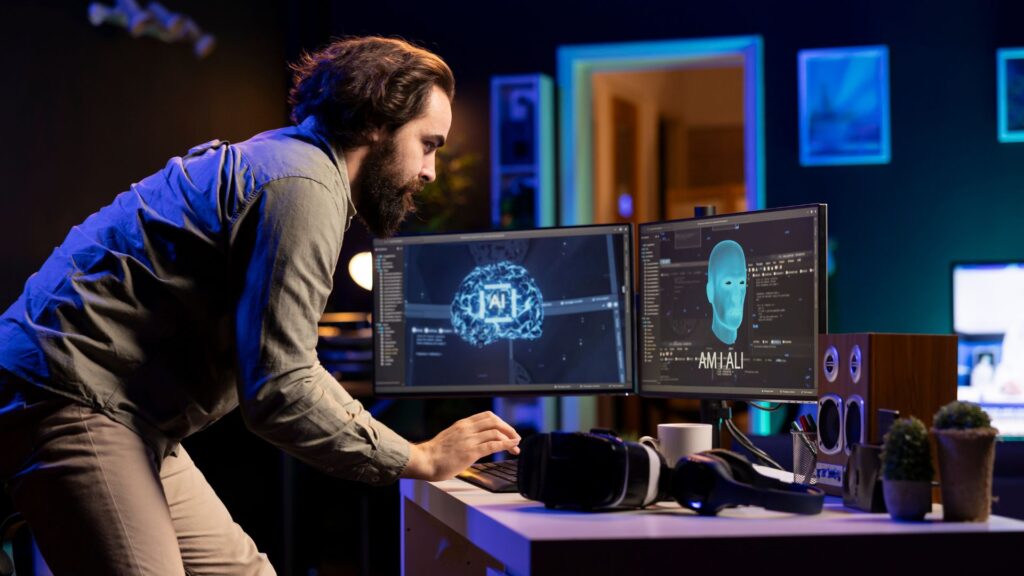 A man stands at a desk using a keyboard and looking at two computer monitors displaying AI, facial recognition graphics, and AI Animation Explainer visuals in a dimly lit office.