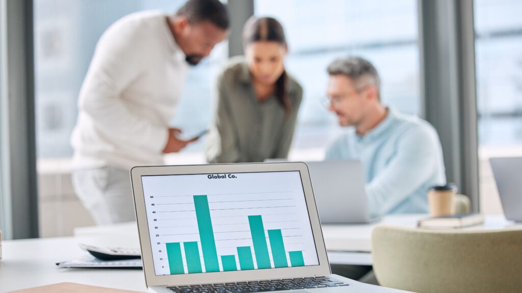 A laptop displays a bar graph labeled “Global Co.” on a desk, while three people collaborate in an office—an ideal scene for creating engaging video content or an AI animation explainer to showcase business insights.