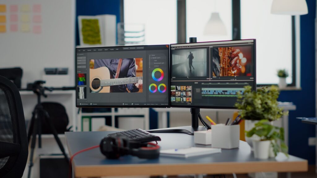 A modern desk with dual monitors displaying video editing software featuring animation elements, a keyboard, headphones, and office supplies in a well-lit room.
