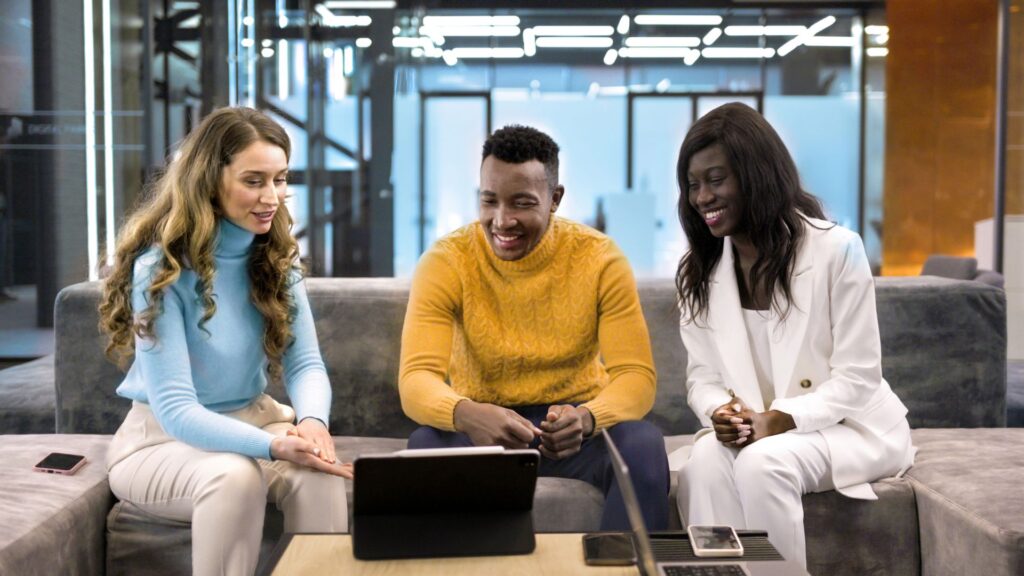 Three people sit on a couch in an office, smiling as they review a SaaS product animation on the tablet. Laptops and notebooks are on the table, reflecting their focus on growth and conversions.