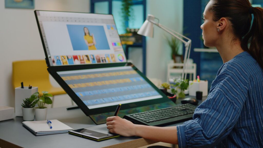 A person sits at a desk in a modern office, using a large touchscreen computer and stylus to edit photos as part of the Priority Animation Project.