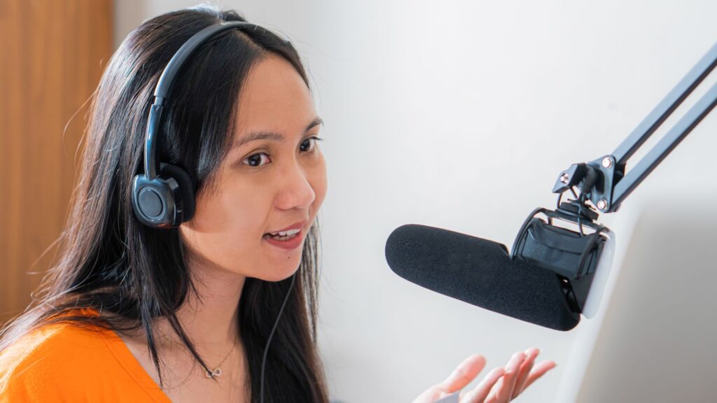 A woman wearing headphones speaks into a microphone, gesturing with her hand in what appears to be an Animation For YouTube Channel recording or podcasting setup.