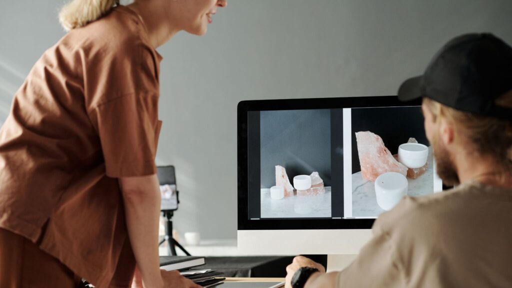 Two people browse product photos of cups and salt lamps on a computer screen in a modern workspace, exploring ideas for their Small Business Animation Services.