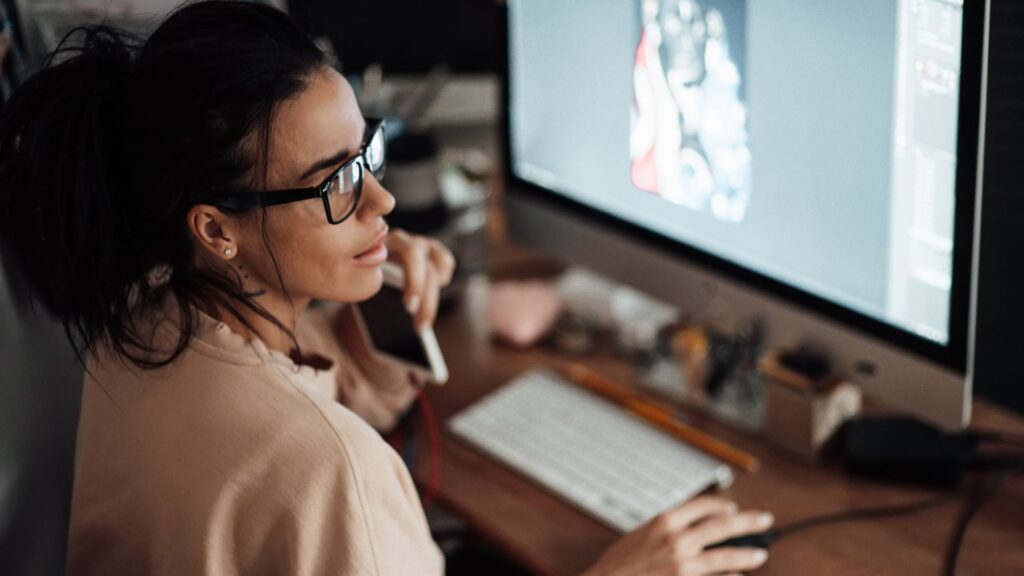 A person wearing glasses works at a desk, using a computer with a stylus and graphics tablet, while talking on the phone about Expedited Animation Services.
