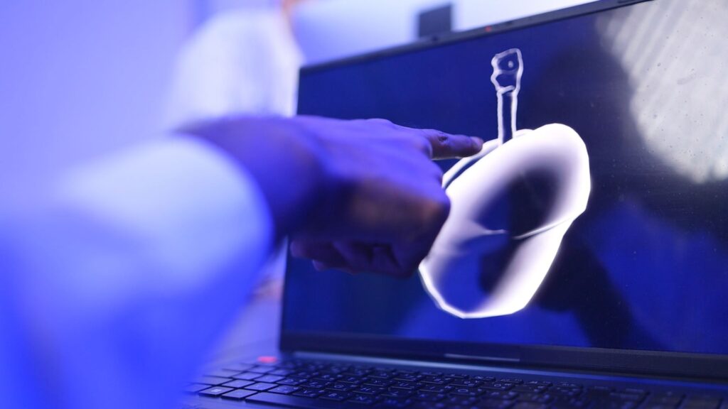 A person points at a digital 3D model of an organ, possibly a liver, displayed on a laptop screen in a blue-lit environment, showcasing medical animation best practices.