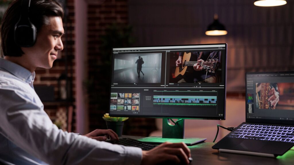 Person wearing headphones edits a 3D video on a desktop computer with dual screens, showing multiple video clips and timelines in a modern workspace—perfect for animation agencies and creative professionals.