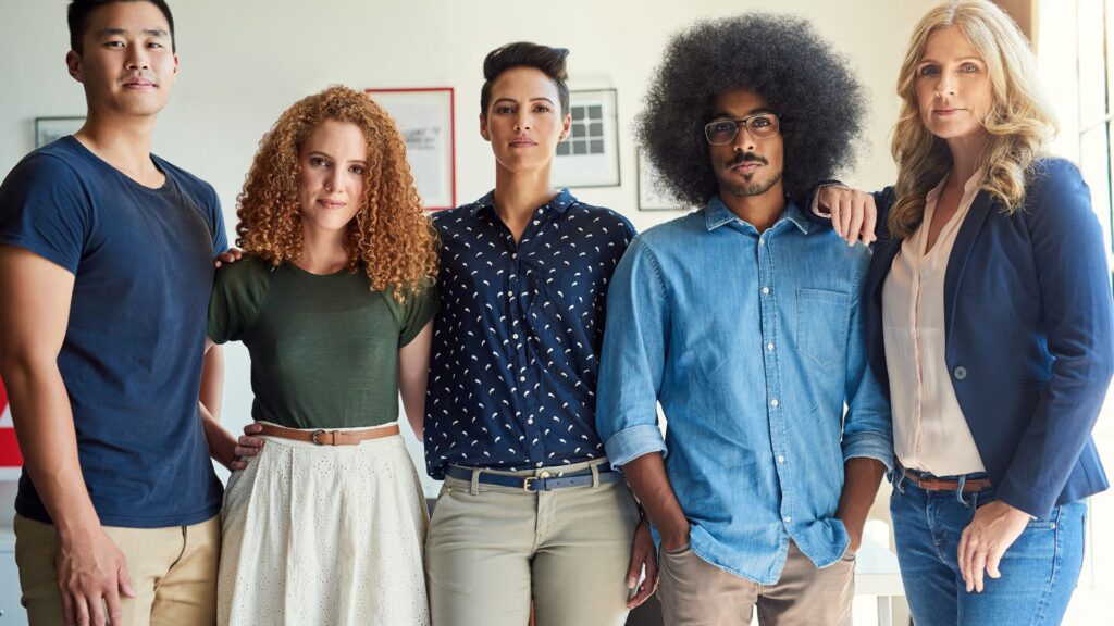 Five people stand indoors in a row, casually dressed, looking at the camera. The bright background and framed pictures on the wall hint at a creative space—perhaps during the Rush Animation Project.