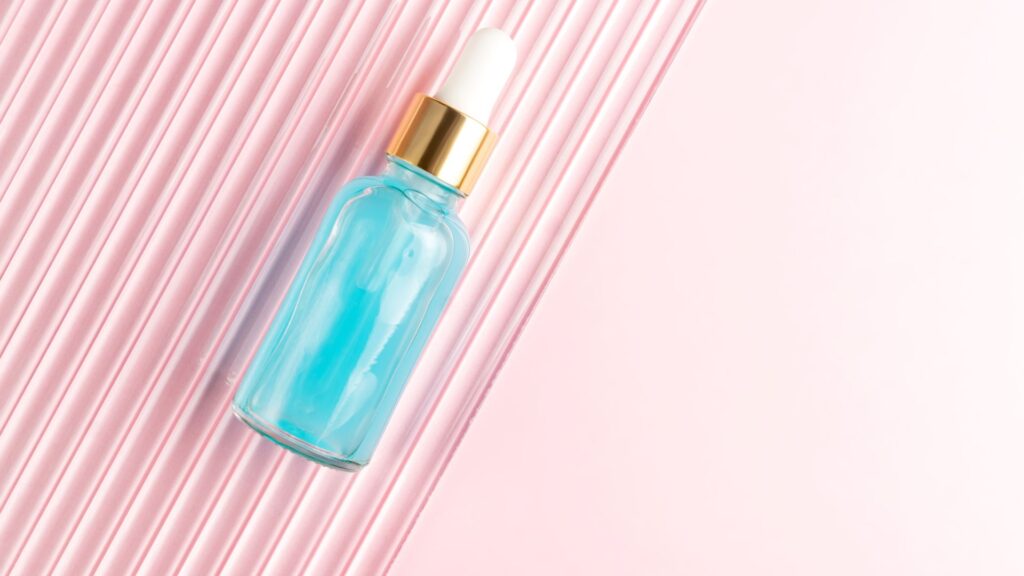 A blue glass dropper bottle with a gold cap and white pipette is placed on a pink textured surface, reminiscent of scenes from a product explanation animation.