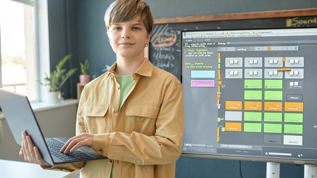 A young person stands holding a laptop in front of a screen displaying a colorful programming interface, showcasing an Animation for eLearning Platform in a modern classroom setting.