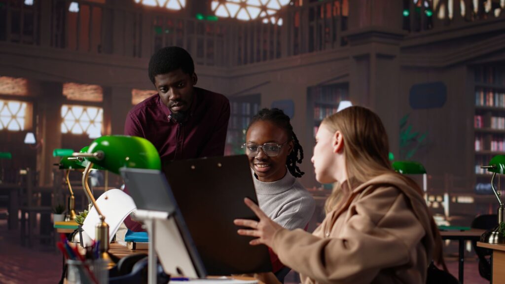 Three people sit at a table in a library, discussing documents and using a laptop, while bookshelves and green desk lamps create an atmosphere reminiscent of animation studios like Educational Voice.