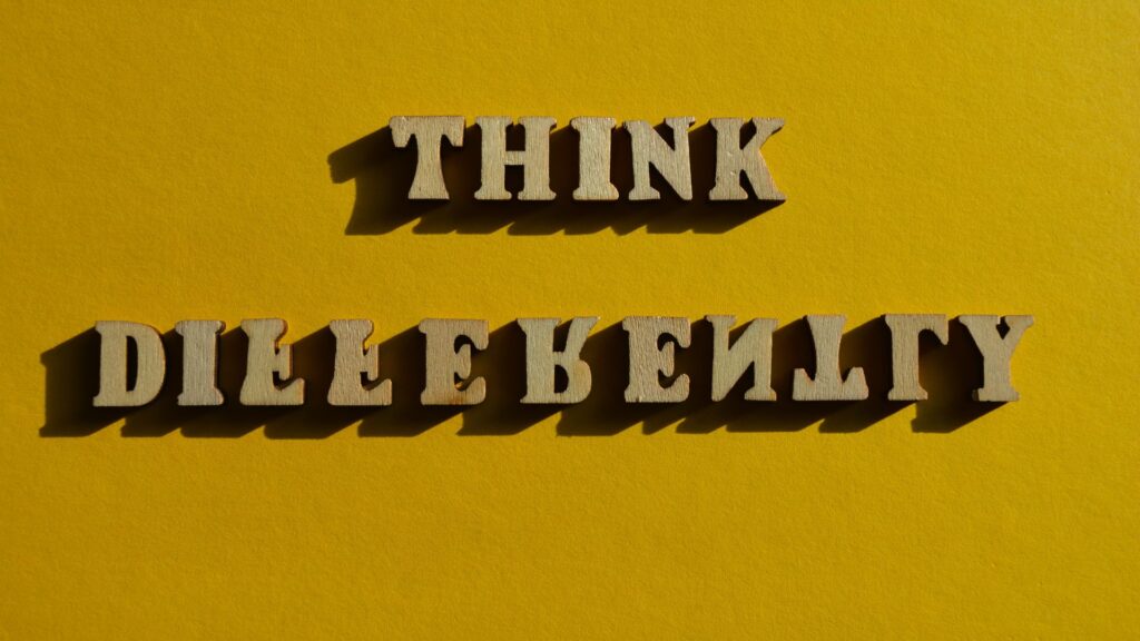 Wooden letters on a yellow background spell out "THINK DIFFERENTLY," but the word "DIFFERENTLY" is misspelled as "DILLE RELLT Y." This playful error could inspire kinetic typography animation techniques popular in the UK.