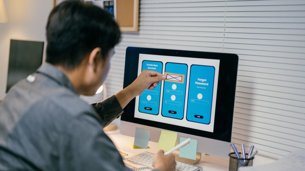 A person designs a mobile app interface on a desktop computer, using a stylus to adjust a wireframe of sign-in and account creation screens with integrated animation for mobile app transitions.