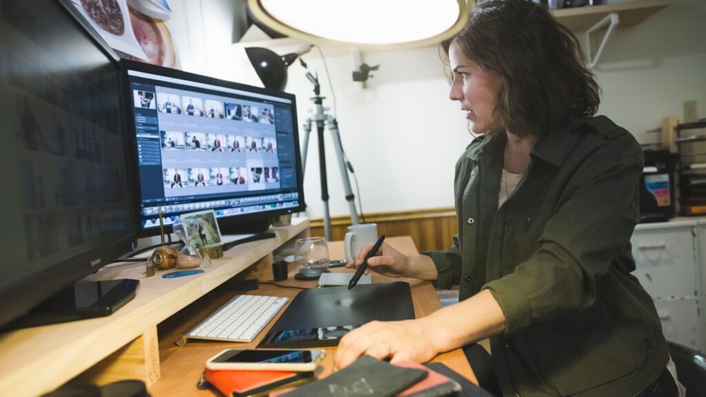 A person edits photos on a computer using a pen tablet at a desk with a keyboard, phone, and camera equipment nearby—referencing an animation value guide can help compare editing tools or understand animation pricing UK.